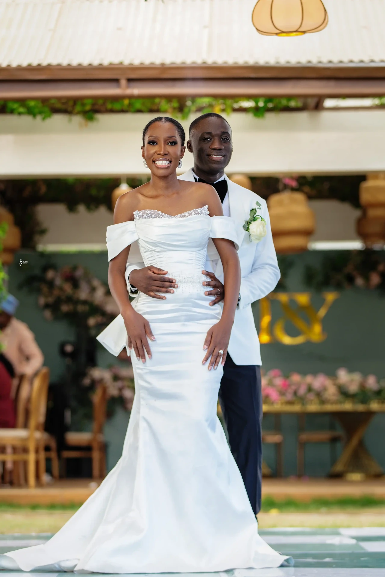 Bride and groom posing together in front of their gold wedding monogram